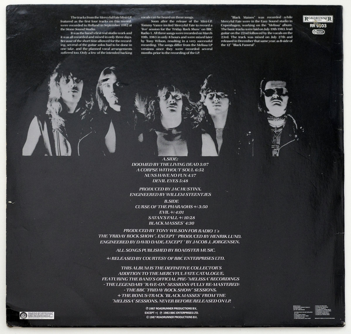 Back cover of Mercyful Fate’s “The Beginning” album. Features a high-contrast black-and-white photograph of the band members, including King Diamond in sunglasses and dark makeup. The musicians stand against a black background with serious expressions. Above the image, text provides background information on the album’s recordings, while below, the tracklist, production credits, and Roadrunner Records logo (RR 9603) are displayed.